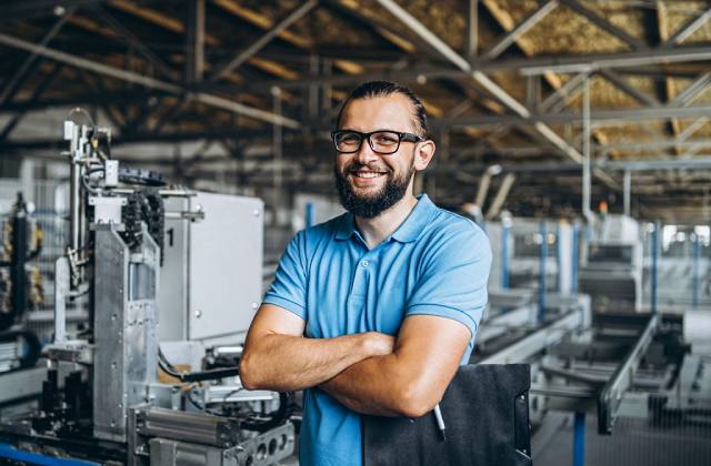 Young engeneer manager with beard checking manufactory, workplace and machinery in big factory